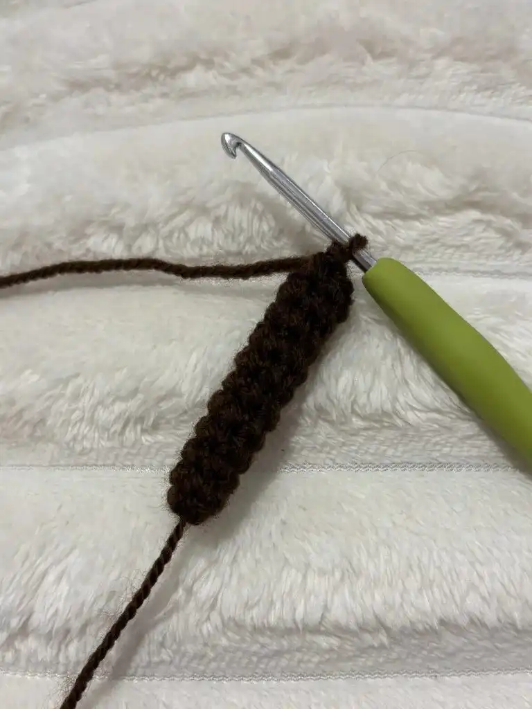 A small, brown crocheted object with a curved shape, showing the stem in progress before stuffing and final shaping.