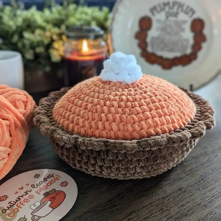 Side view of the crocheted pumpkin pie, highlighting the distinct layers of the orange filling, tan crust, and the overall plush texture.