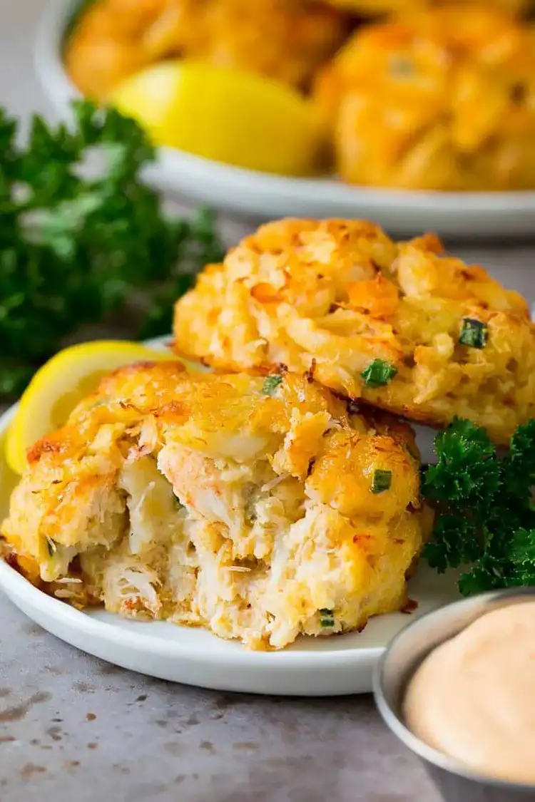 Two beautifully seared Maryland Crab Cakes on a plate, garnished with fresh herbs and a slice of lemon.