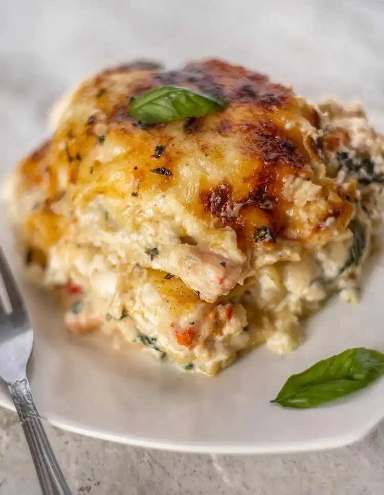 A generous slice of Seafood Lasagna showing layers of pasta, creamy sauce, cheese, and various seafood pieces.