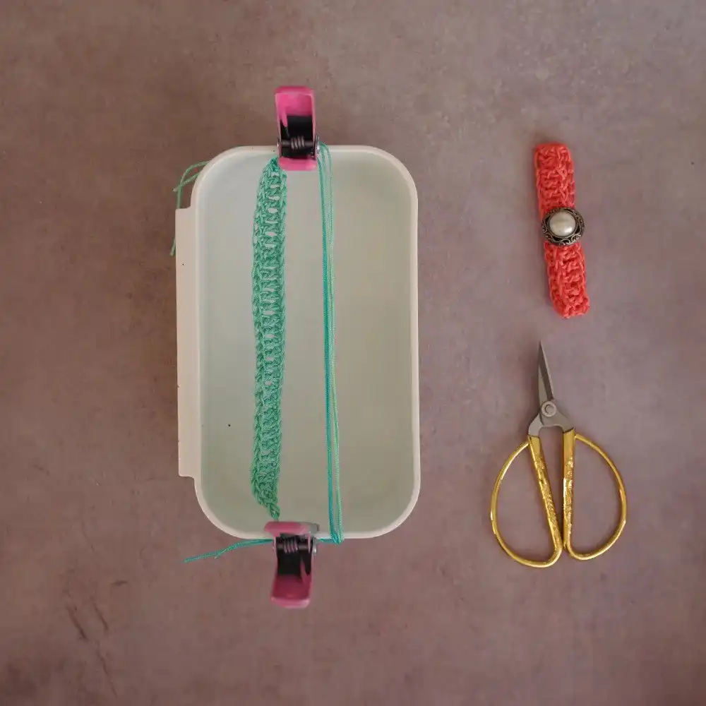 A double crochet bracelet with a button closure, alongside golden embroidery scissors and a crochet hook, on a grey surface.