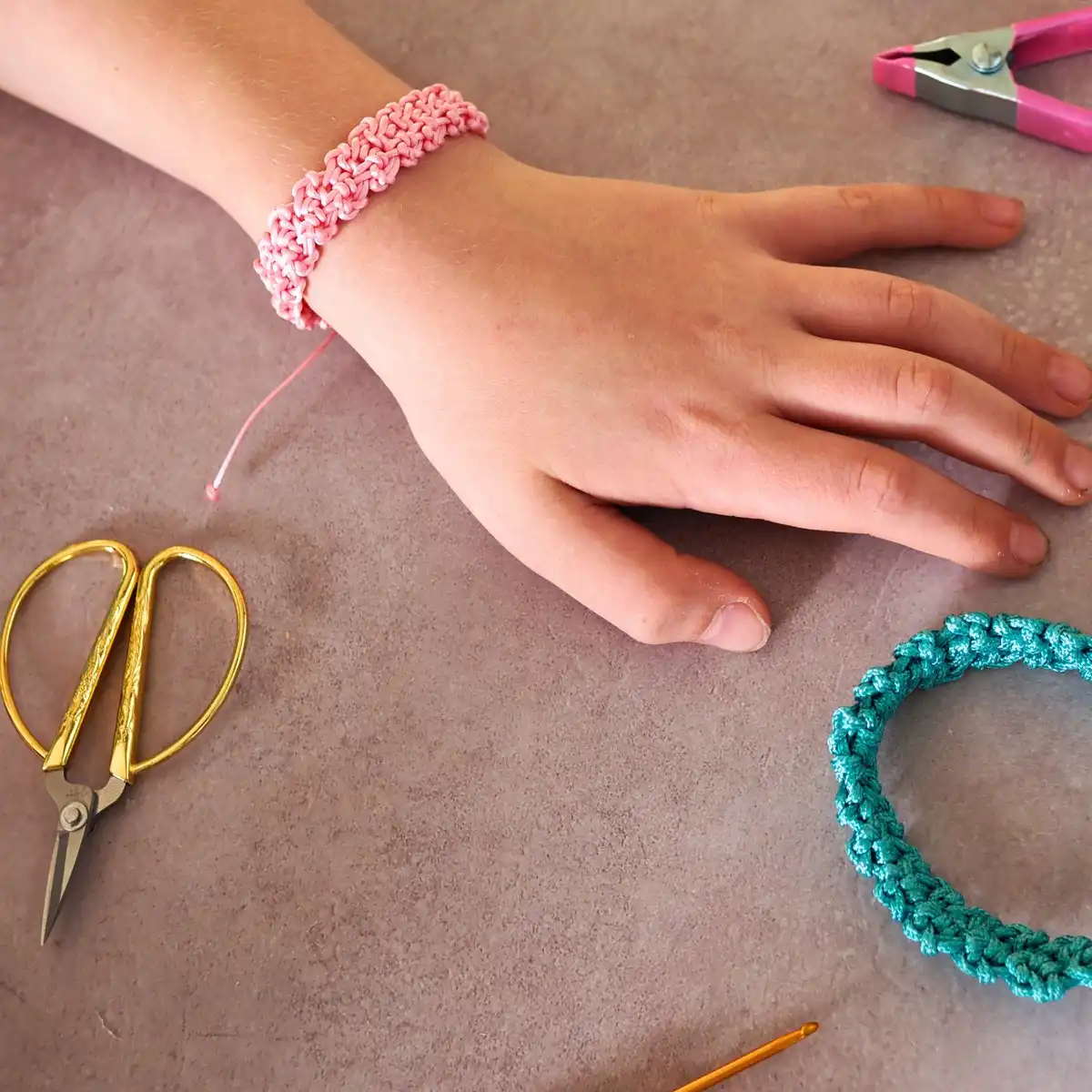 Crafting materials for a Single Crochet Stitch Friendship Bracelet, including crochet hooks, colorful cords, beads, and scissors, arranged neatly.