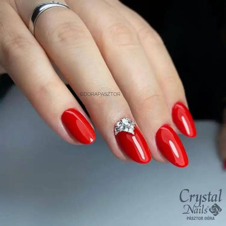 Glossy red acrylic nails adorned with sparkling rhinestones on accent fingers, adding elegance and bling.