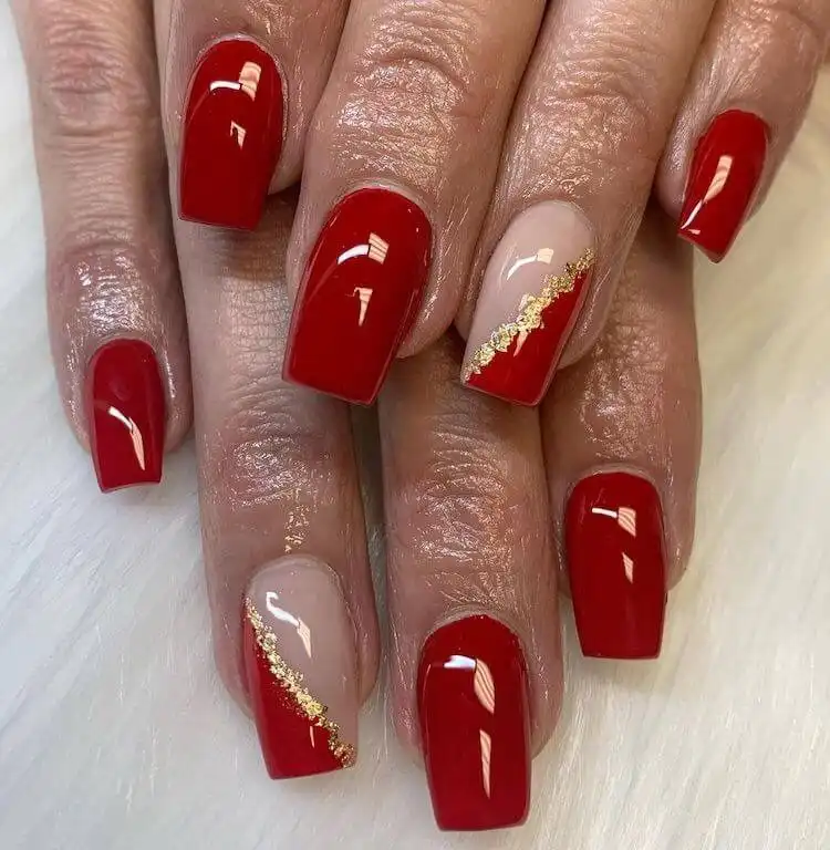 Simple yet chic red acrylic nails with delicate gold foil flakes on the ring finger, adding a touch of luxury.