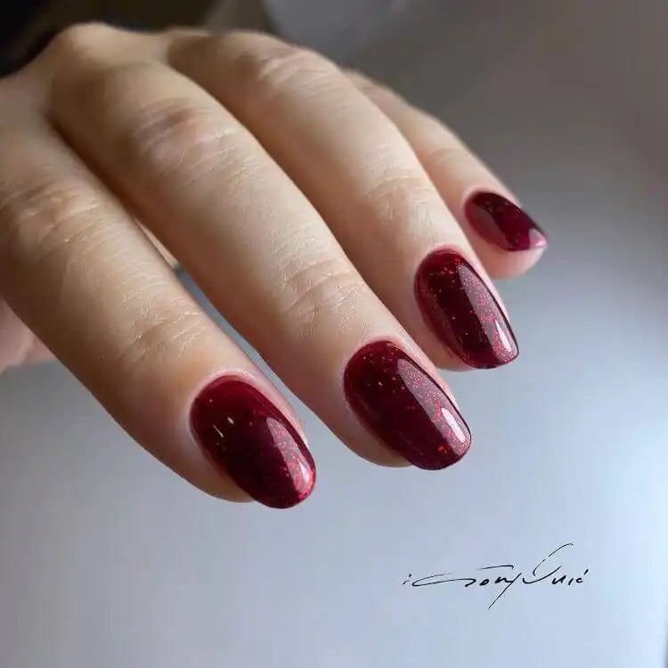 Deep red glitter acrylic nails layered over black polish, creating a rich, multi-dimensional effect and depth.