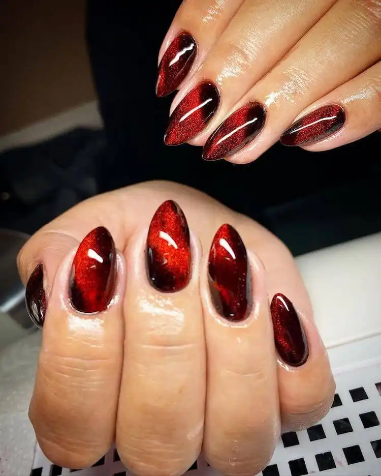 Red and black cat eye acrylic nails with a sharp diagonal magnetic line, showcasing a unique nail trend.