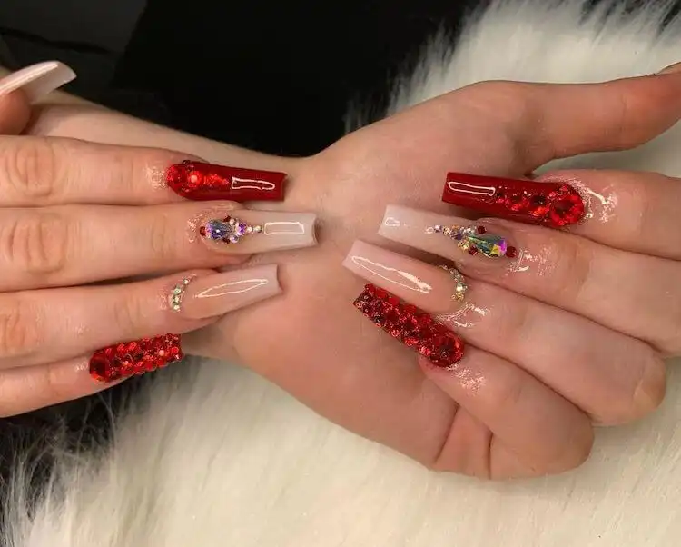Extremely blinged out red acrylic stiletto nails with heavy rhinestone embellishments for a glamorous statement.