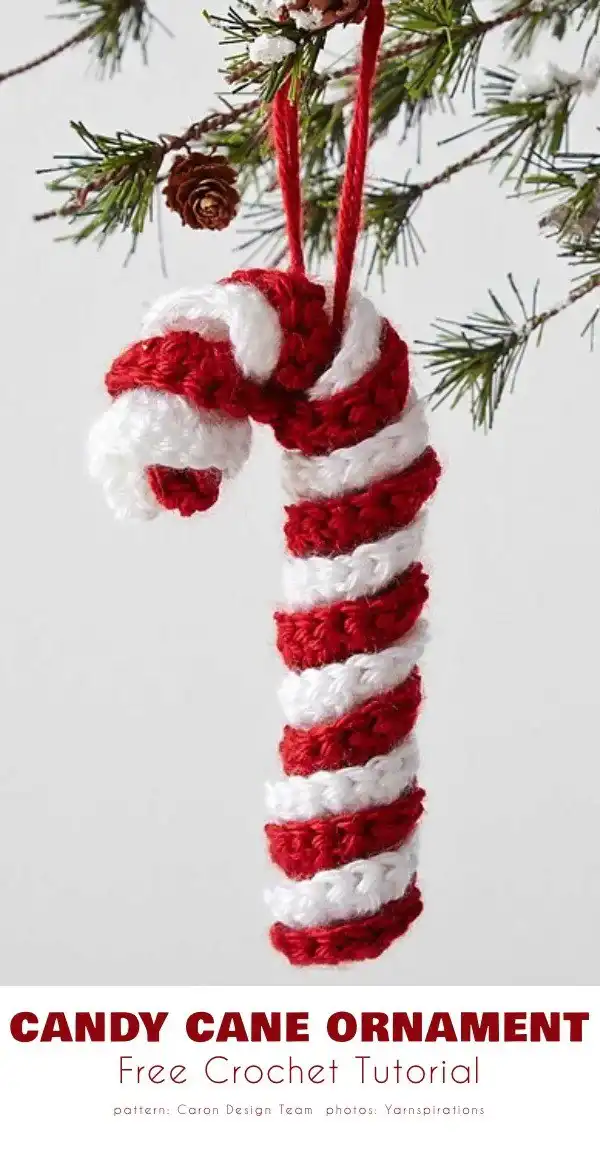 A 3D crocheted candy cane ornament, featuring traditional red and white spirals, hanging on a Christmas tree branch.