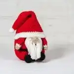 Two crocheted Christmas Gnome figures with red hats and white, curly beards, nestled among gifts and pinecones.