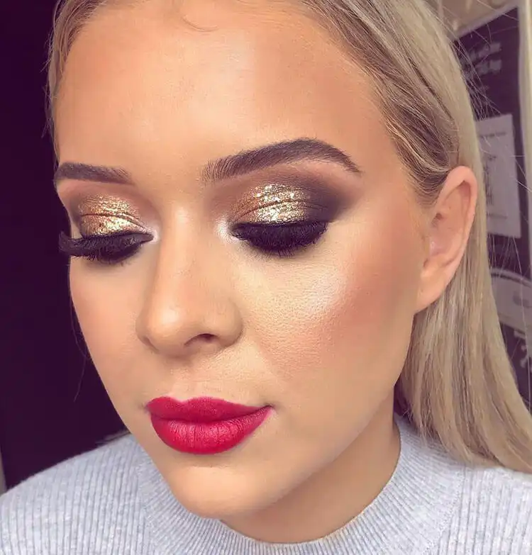 A model with glamorous gold glitter eye makeup paired with a classic bold red lipstick.
