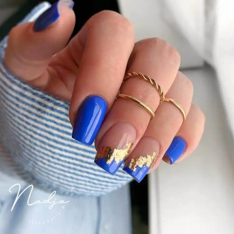 Luxurious royal blue gel nails in a square shape with gold flake accents, a wonderful blue nail design that is bold and classic.