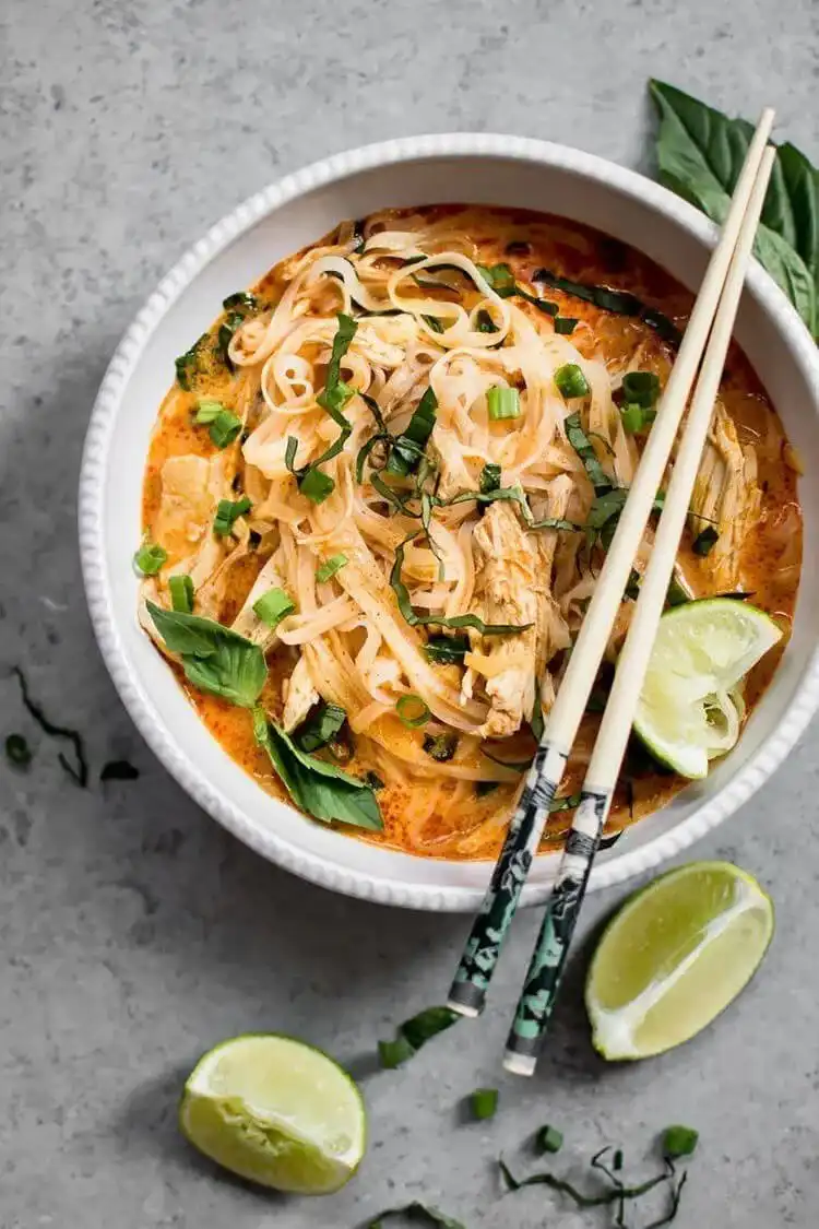 A bowl of 20-minute Thai chicken curry soup, vibrant with coconut milk, curry broth, chicken, and fresh herbs.
