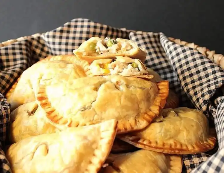 Golden-brown chicken pot pie turnovers on a baking sheet, showing flaky crusts and savory filling.