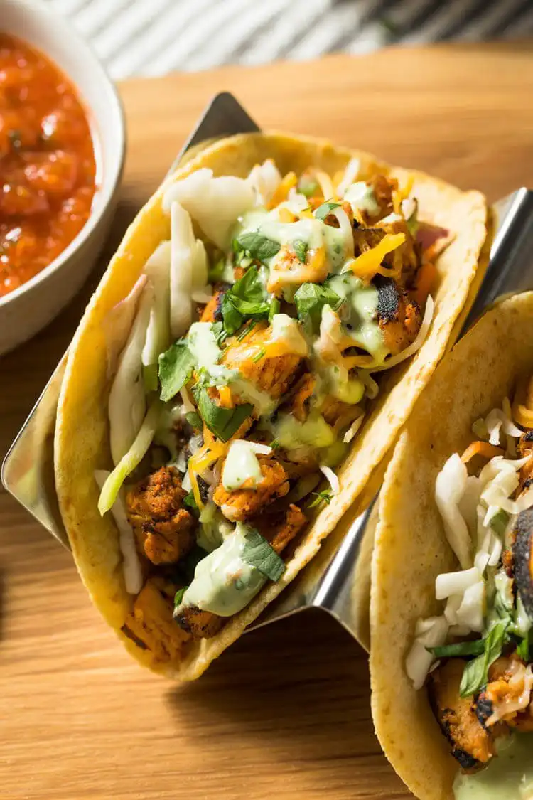 An array of easy rotisserie chicken tacos, filled with shredded chicken and various fresh toppings like salsa and avocado.