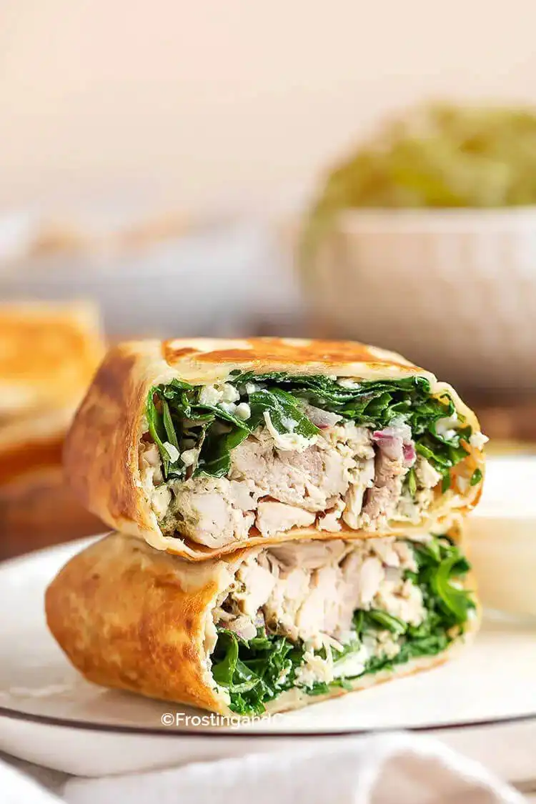 Fresh pesto chicken wraps filled with shredded rotisserie chicken, arugula, feta, and red onion, drizzled with lemon garlic yogurt sauce.