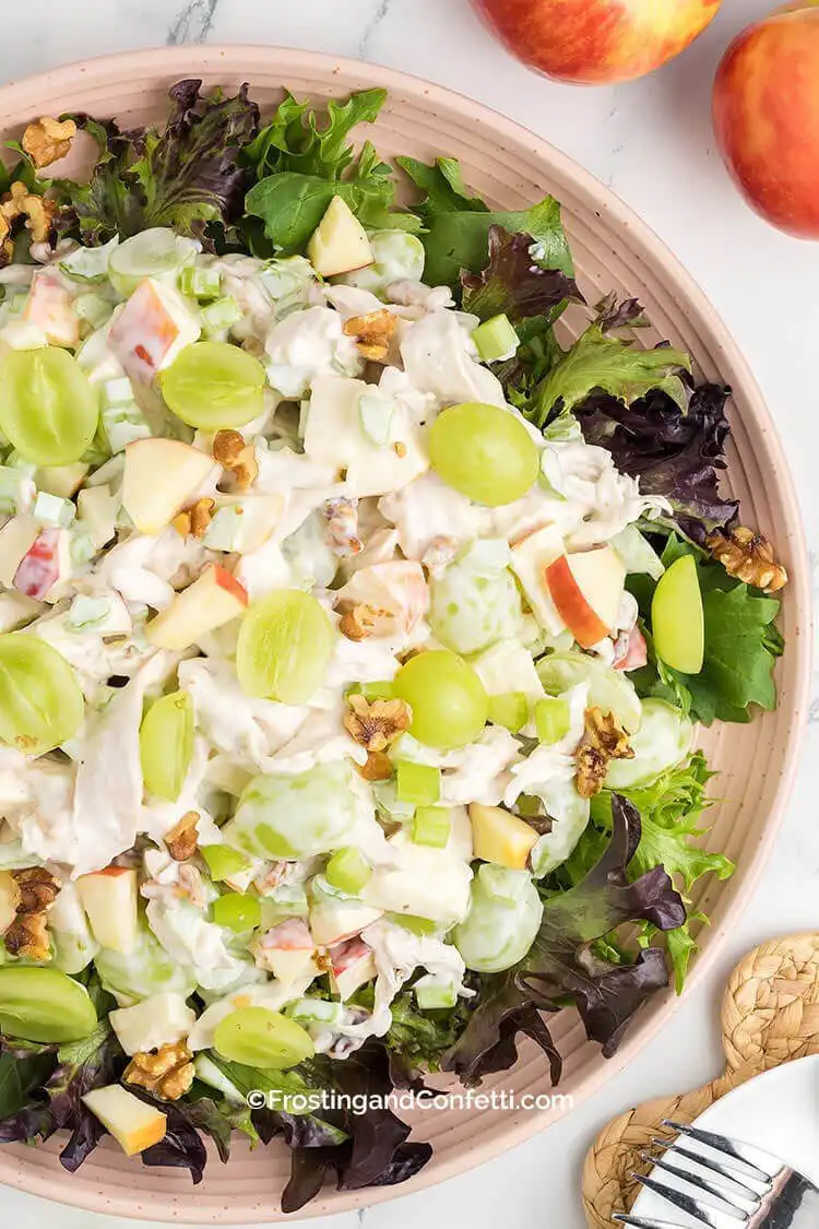 A fresh Waldorf chicken salad in a bowl, featuring shredded rotisserie chicken, apples, grapes, celery, and walnuts.