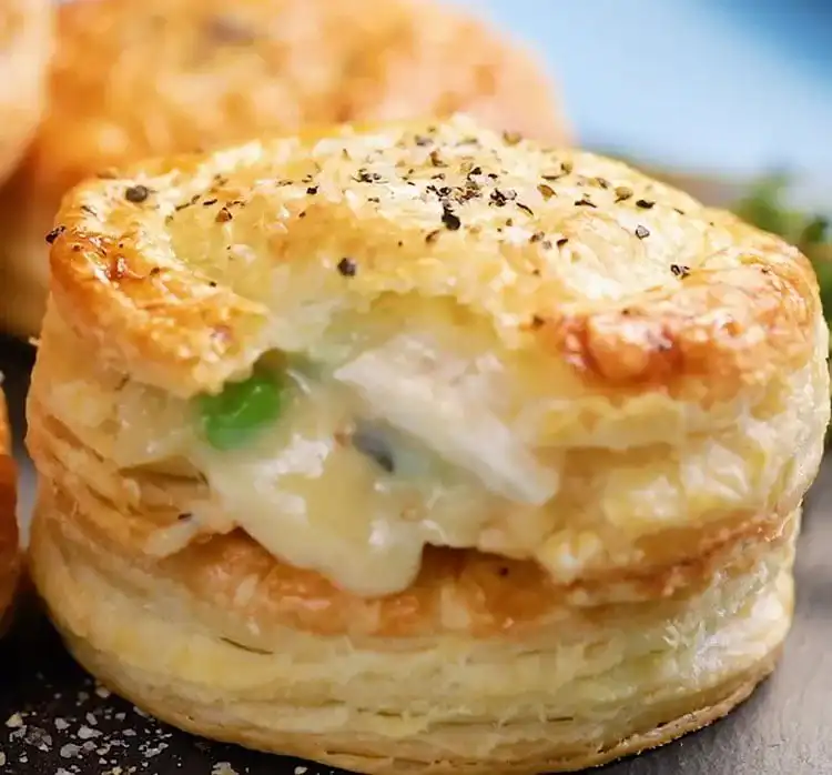 Individual chicken pot pie biscuits baked in muffin tins, with a golden biscuit top revealing a creamy chicken and vegetable filling.